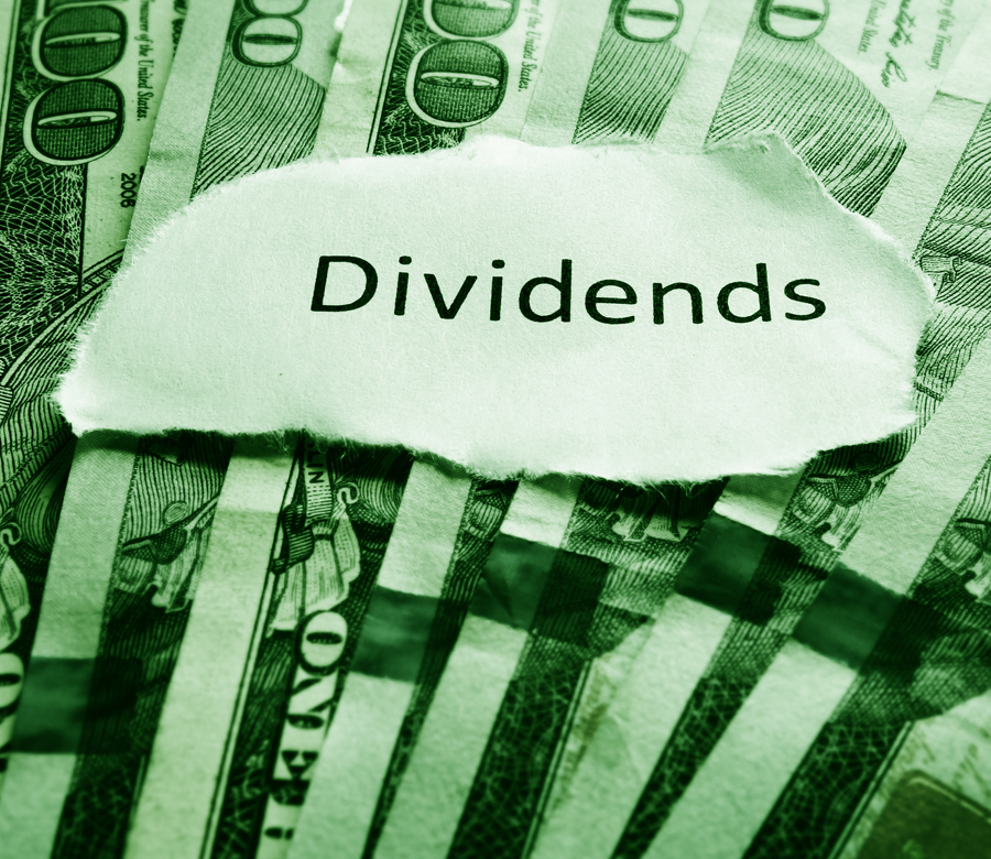Ripped piece of paper with text dividends on top of money.