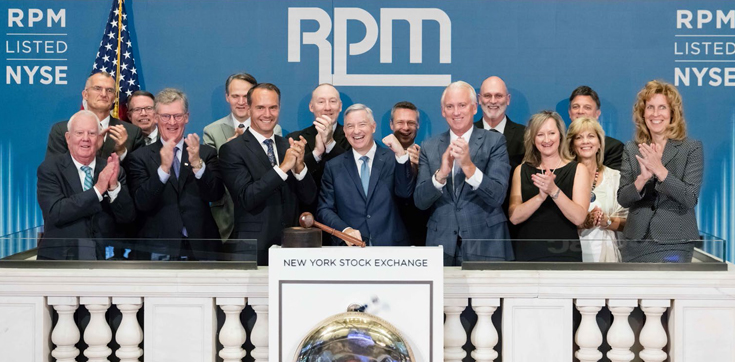 Group of people standing in front of a blue background at the NYSE with the RPM logo.